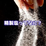 手から落ちる白い塩の粒と「精製塩ってない？」という文字が入ったイメージ
